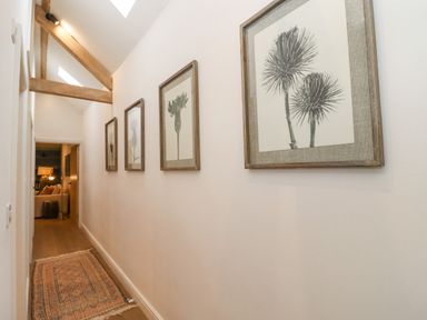 A hallway with wooden beams on the ceiling a narrow rug on the floor and framed botanical prints on the wall at Hawthorn Barn in Northleach