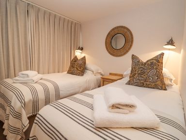 A bedroom with two single beds with patterned pillows and folded towels at Hawthorn Barn in Northleach