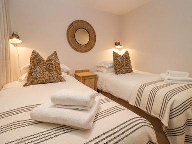 A bedroom with two single beds, patterned cushions, a wooden side table, and wall lamps at Hawthorn Barn in Northleach