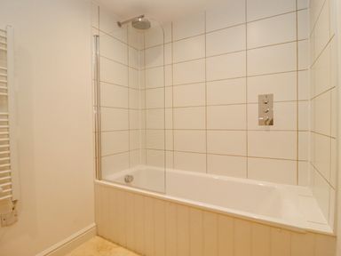 A bathroom with a bathtub shower combination and a glass shower screen at Hawthorn Barn in Northleach