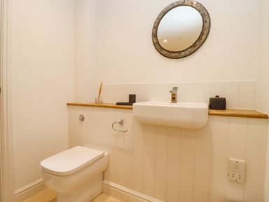 A bathroom with a wall-mounted sink a toilet and a round mirror at Hawthorn Barn in Northleach