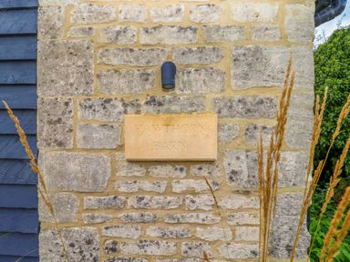 A stone wall with a sign reading Hawthorn Barn surrounded by plants at Northleach