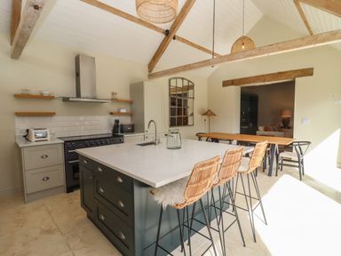 A kitchen with an island and bar stools next to a dining table and chairs at Hawthorn Barn in Northleach