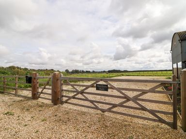 A wooden gate with a sign reading Hawthorn Barn opening onto a gravel driveway and fields at Hawthorn Barn in Northleach