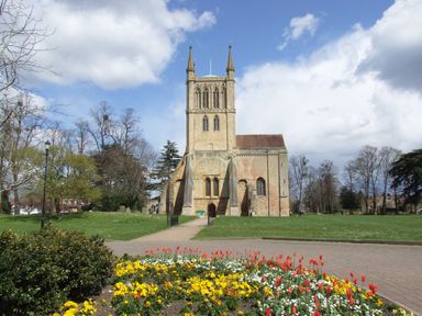 A church with twin spires surrounded by grass trees and flowers at The Cotswold Holiday Lodge in Evesham