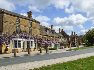 A street with old stone buildings covered with purple flowers and a grassy area at The Cotswold Holiday Lodge in Evesham