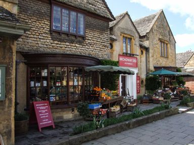 A street view of a deli with fruit and vegetable stands outside in front of stone buildings at The Cotswold Holiday Lodge in Evesham