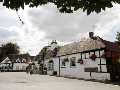 An exterior view of a traditional inn with hanging flower baskets and a sign at The Cotswold Holiday Lodge in Evesham