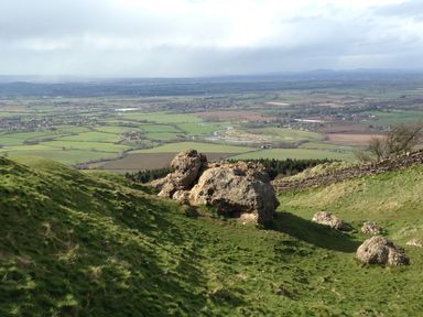 A view of green fields and farmland from a hillside with large rocks in the foreground