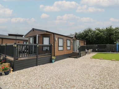 A mobile home with a deck and lawn at The Cotswold Holiday Lodge in Evesham