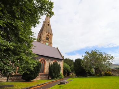 A stone church building with a clock tower surrounded by trees and grass at Dove Cottage in Ruthin