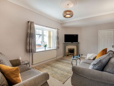 A living room with two sofas a fireplace a television and a window with curtains at Dove Cottage in Ruthin