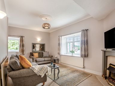 A living room with two sofas a small table a window with curtains and a fireplace at Dove Cottage in Ruthin
