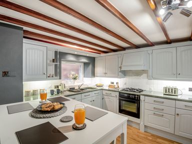 A kitchen with white cabinets wooden ceiling beams and a white table with pastries and orange juice at Dove Cottage in Ruthin