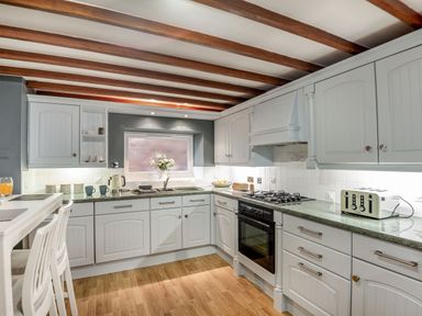 A kitchen with white cabinets a green countertop a gas stove a toaster a sink and two white chairs at Dove Cottage in Ruthin