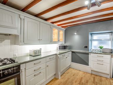 A kitchen with white cabinets gray walls wooden ceiling beams and a microwave on the countertop at Dove Cottage in Ruthin