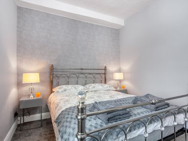 A bedroom with a metal bed frame two bedside tables with lamps and orange drinks at Dove Cottage in Ruthin