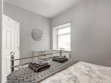 A bedroom with a bed and folded towels a window with blinds a mirrored drawer and a door at Dove Cottage in Ruthin
