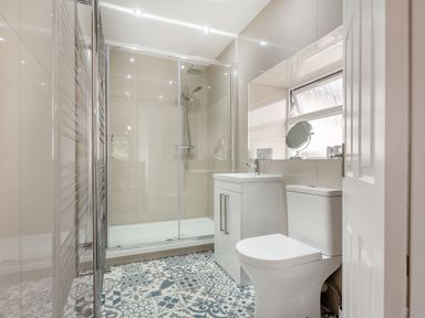 A bathroom with a shower enclosure sink and toilet with patterned floor tiles at Dove Cottage in Ruthin