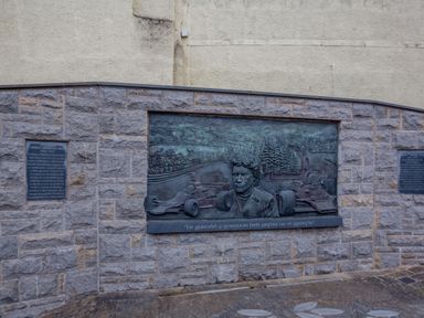 A stone wall with a bronze memorial plaque showing a man and race cars with inscriptions at Dove Cottage in Ruthin