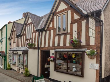 A street view of a timber-framed building with hanging flower baskets and display windows at Dove Cottage in Ruthin
