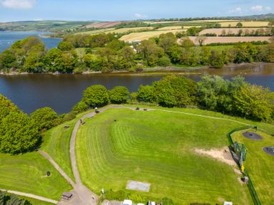A green park with pathways benches and a playground near a river with trees and fields beyond at Teifi Villa in St Dogmaels