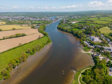 An aerial view of a river flowing through green fields and a small town with boats on the water at Teifi Villa in St Dogmaels
