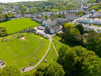 A large green park with picnic benches and pathways next to residential houses and buildings in a village