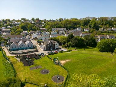 A playground with swings and climbing equipment next to houses and a park in a residential area at Teifi Villa in St Dogmaels