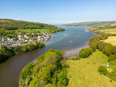 A river bordered by green fields and a village with boats on the water at Teifi Villa in St Dogmaels