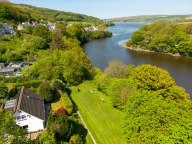 A river bordered by trees and green hills with houses visible in the background at Teifi Villa in St Dogmaels