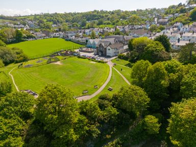 A park with playground equipment benches and a pathway surrounded by trees near houses in Teifi Villa St Dogmaels