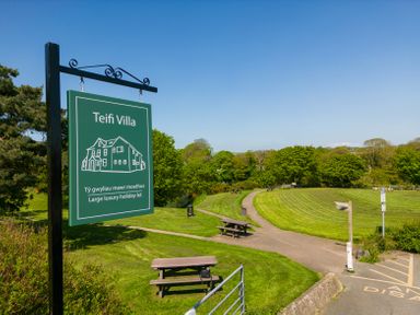A green sign for Teifi Villa with picnic benches and a path in a grassy park area at Teifi Villa in St Dogmaels