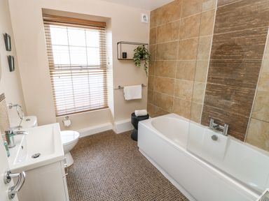 A bathroom with a bathtub a sink a toilet a window with blinds and a towel rack at Teifi Villa in St Dogmaels