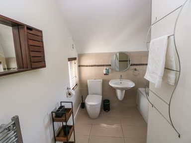 A bathroom with a toilet sink mirror small window towel rack and shelving unit at Teifi Villa in St Dogmaels