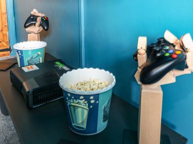Two popcorn containers and gaming controllers held by wooden hand sculptures on a black table with a black device at Teifi Villa in St Dogmaels
