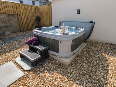 An outdoor hot tub with steps and purple towels on a gravel surface with a wooden fence and stone wall in the background at Teifi Villa in St Dogmaels