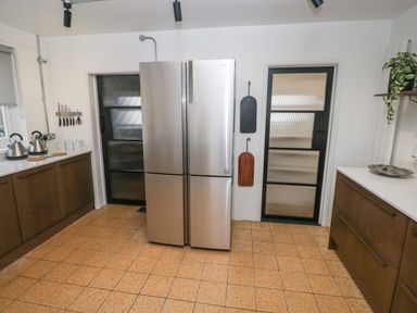 A kitchen with a stainless steel refrigerator two black framed glass doors wood cabinets kettles and knives on the wall at Teifi Villa in St Dogmaels