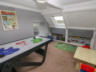 A playroom with an air hockey table a small table with two chairs a toy storage unit a play mat and a framed beano comic on the wall at Teifi Villa in St Dogmaels
