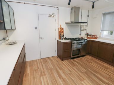 A kitchen with wooden cabinets a stainless steel stove and oven wooden floor and white countertops at Teifi Villa in St Dogmaels