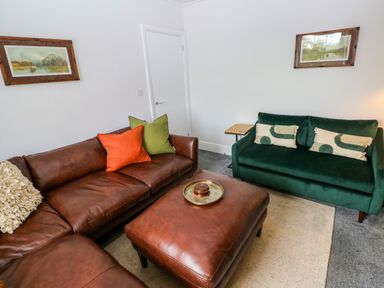 A living room with a brown leather sofa and green sofa at Teifi Villa in St Dogmaels