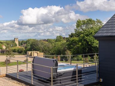 An outdoor deck area with a hot tub surrounded by metal railings and a view of trees and buildings at Foxes Den in Allerston near Thornton Dale