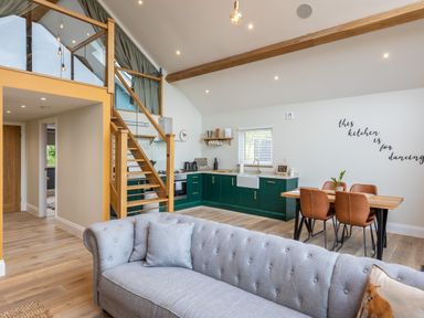 An open plan kitchen and dining area with green cabinets a wooden dining table with four chairs and a gray sofa in the foreground at Foxes Den Allerston near Thornton Dale