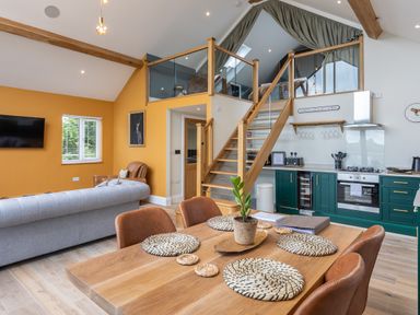 An open plan living area with a dining table and chairs a kitchen with green cabinets and a staircase leading to a mezzanine at Foxes Den in Allerston near Thornton Dale