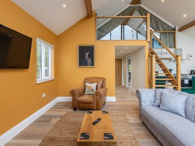 A living room with a brown armchair, gray sofa, wooden coffee table, wall-mounted TV, and staircase at Foxes Den in Allerston near Thornton Dale