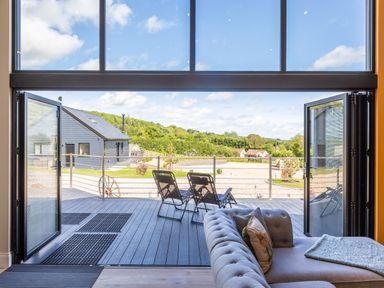 A patio with outdoor chairs and a railing viewed from inside with a grey couch in the foreground at Foxes Den Allerston near Thornton Dale