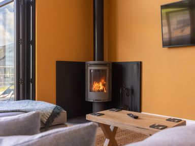 A living room with a wood stove fireplace a wooden coffee table and a wall-mounted television at Foxes Den Allerston near Thornton Dale