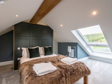A bedroom with a bed covered in a fur throw and towels near a large skylight window at Foxes Den Allerston near Thornton Dale