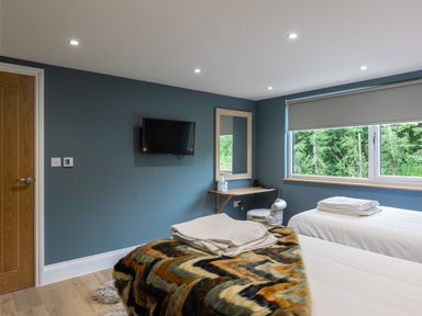 A bedroom with two single beds a wall-mounted tv a window with a roller blind and a small desk with a mirror at Foxes Den Allerston near Thornton Dale