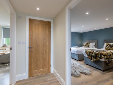 A hallway with a wooden door and two open doorways showing a bedroom with two beds and a bathroom with a bathtub at Foxes Den in Allerston near Thornton Dale